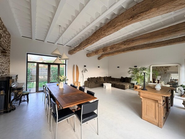 A spacious living area with a wooden dining table, black chairs, a sofa, and a kitchen area with a wooden cabinet.