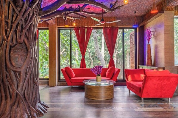 A modern interior with a red sofa, a round wooden coffee table, and a large tree sculpture.
