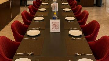 A conference room with a long table set for a meeting, red chairs, a minibar, and a reception area.