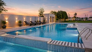 A rectangular swimming pool with a tiled edge, surrounded by lounge chairs and potted plants. - Pallacia A Luxury Hotel (Beawar)