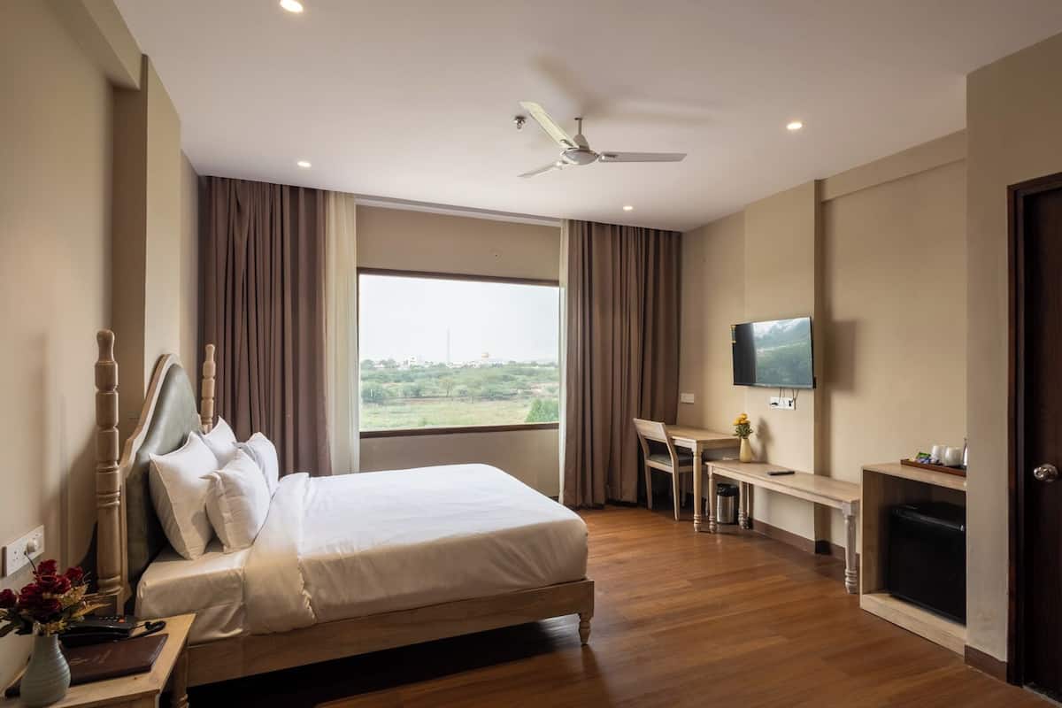 A hotel room with a bed, a desk, a television, and a view of the outdoors.