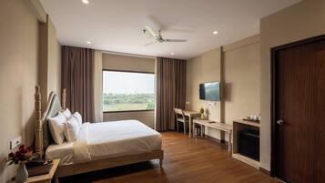 A hotel room with a bed, a desk, a television, and a view of the outdoors.
