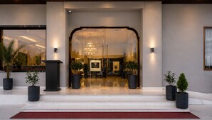 A hotel entrance with a glass door, a reception desk, and potted plants. - Pallacia A Luxury Hotel (Beawar)