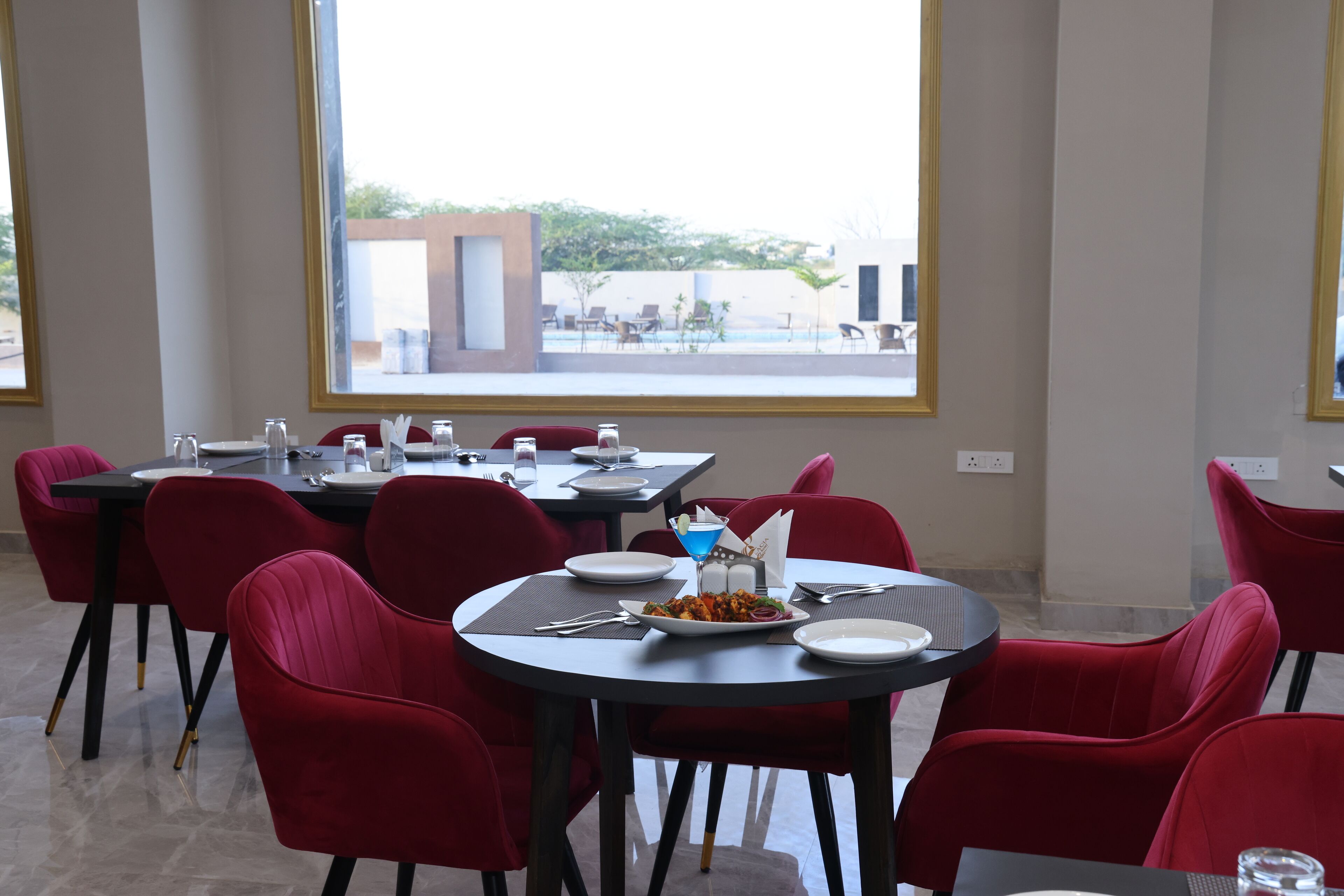 A dining area with red chairs and tables, a plate of food, and a window view of an outdoor area with chairs and a pool.