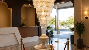 A lobby with a large chandelier, a reception desk, and a patterned floor. - Pallacia A Luxury Hotel (Beawar)