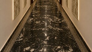 A long, narrow hallway with a polished marble floor, recessed lighting, and framed artwork on the walls. - Pallacia A Luxury Hotel (Beawar)