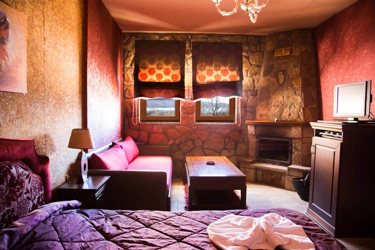 Een knus ingerichte kamer met een bed, een bank, een klein tafeltje, een open haard en een televisie.