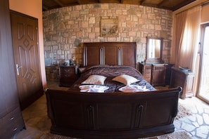 A bedroom with a stone wall, a wooden bed, a nightstand, a dresser, and a mirror. - Silva Suites - Kryoneri, Lake Plastira (Lake Plastiras)