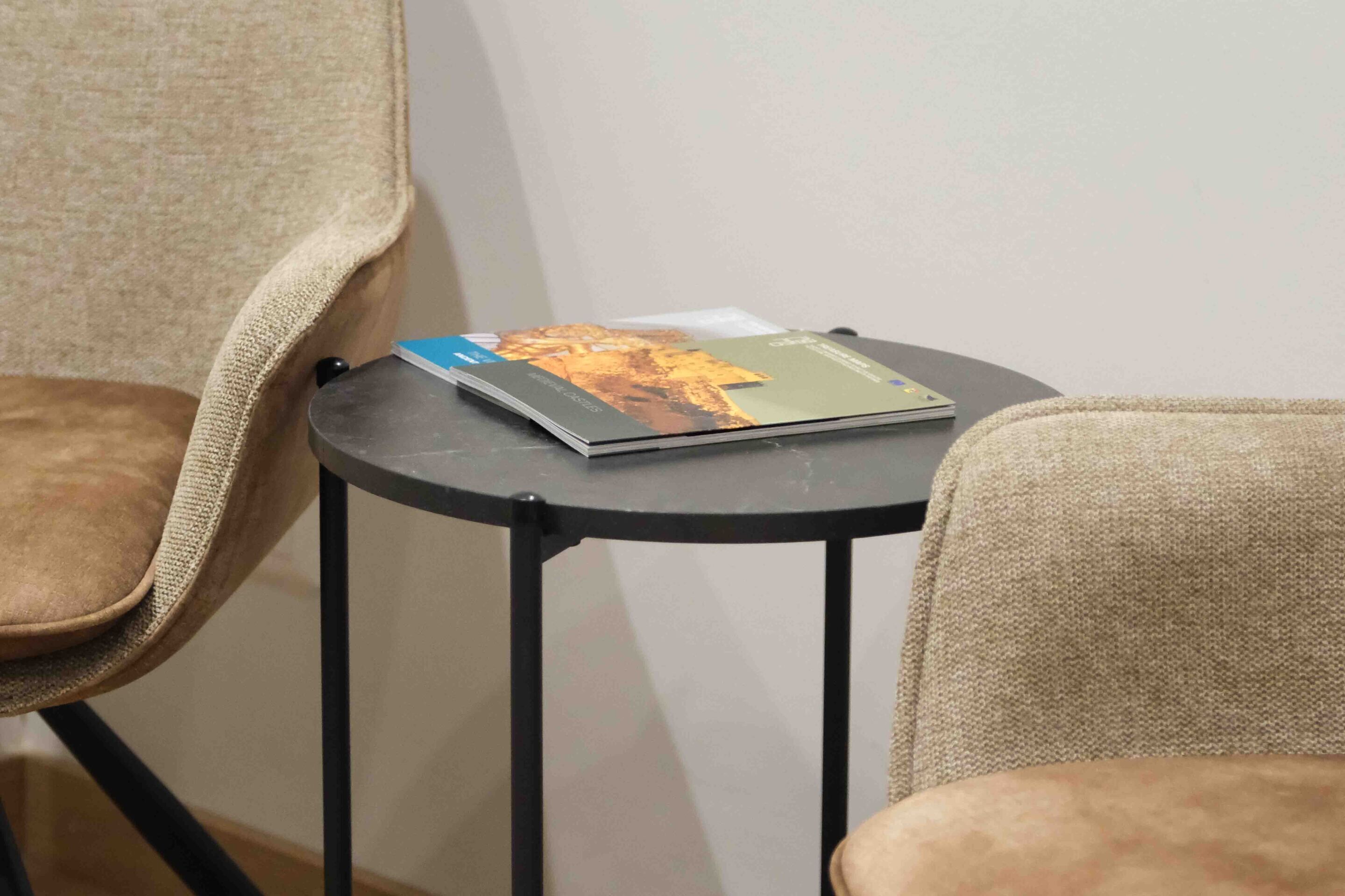 Ett litet runt bord med ett tidskrift på, placerat mellan två beige stolar.