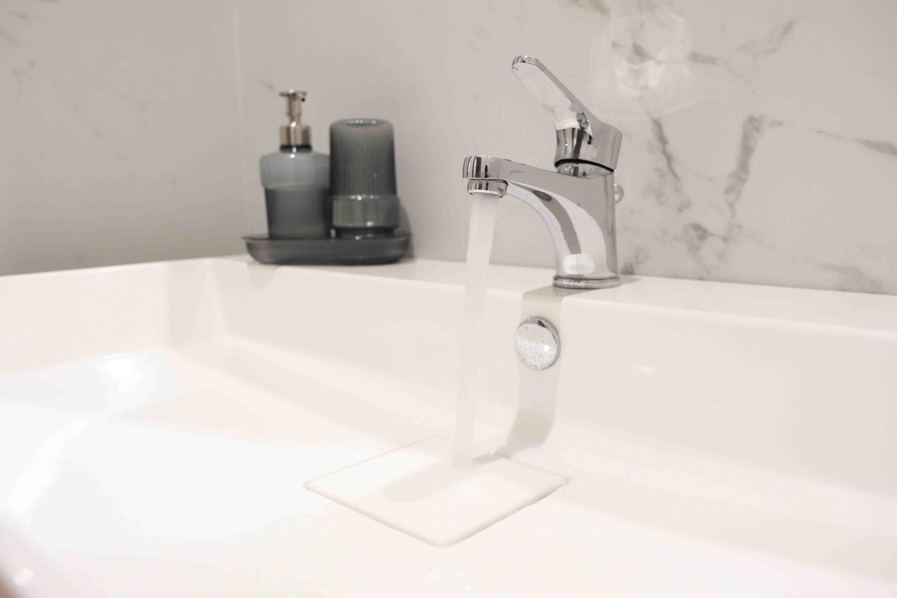 A bathroom with a white sink, a chrome faucet, and two soap dispensers.