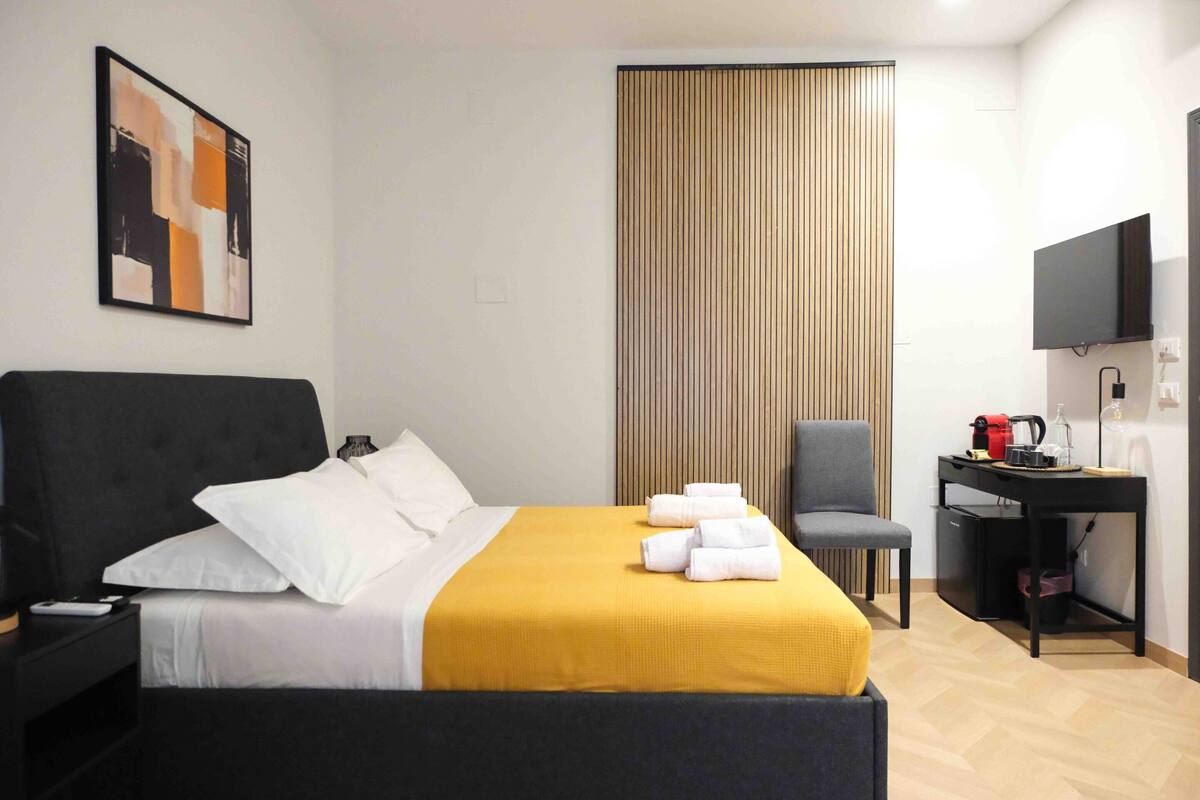 A modern hotel room with a large bed, a desk, a chair, and a television.