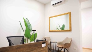 A reception area with a wooden desk, a chair, a small table with a chair, a large mirror, and a potted plant. - Mazzini Suites Palermo (Palermo)