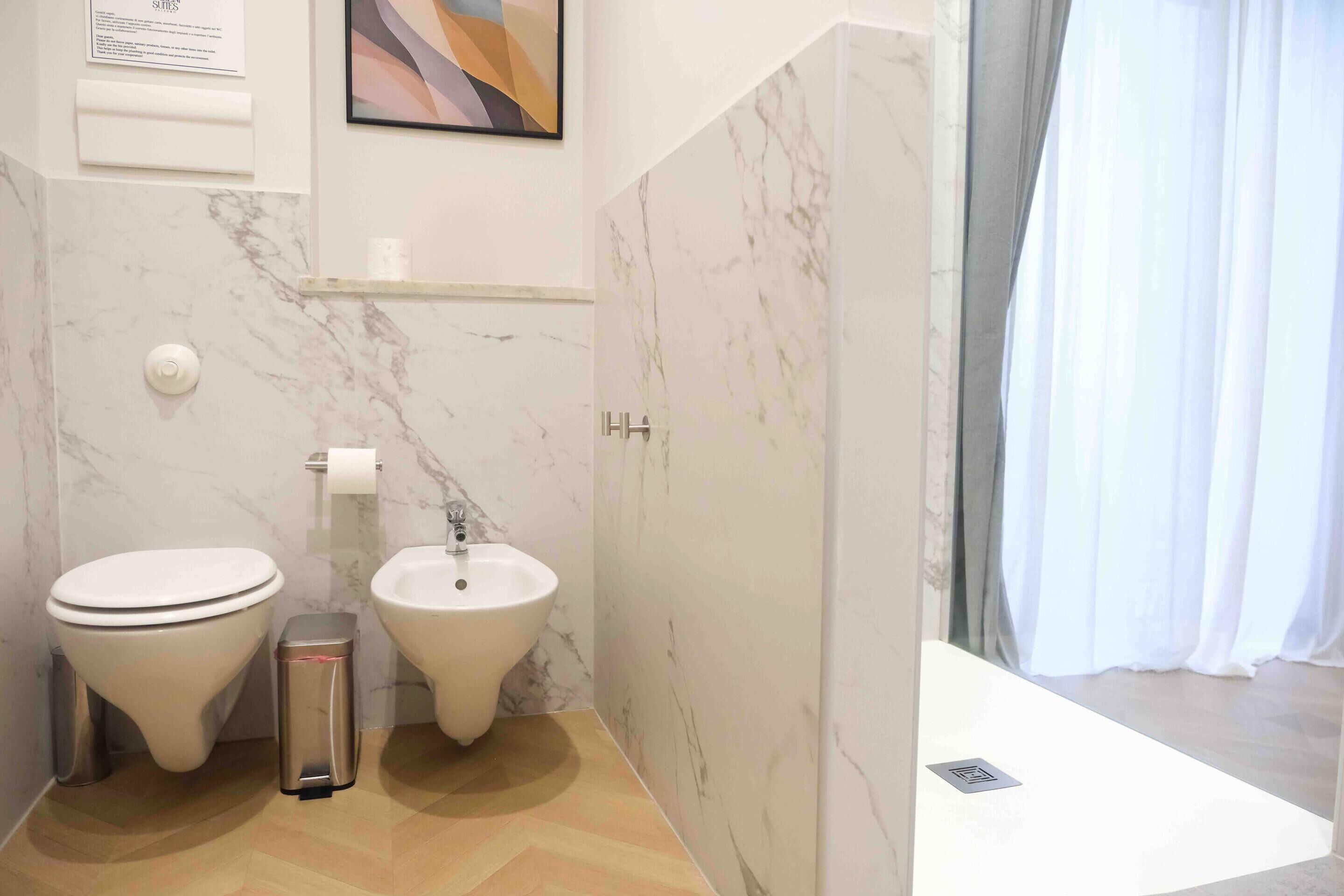 A modern bathroom with a toilet, bidet, and a trash bin.