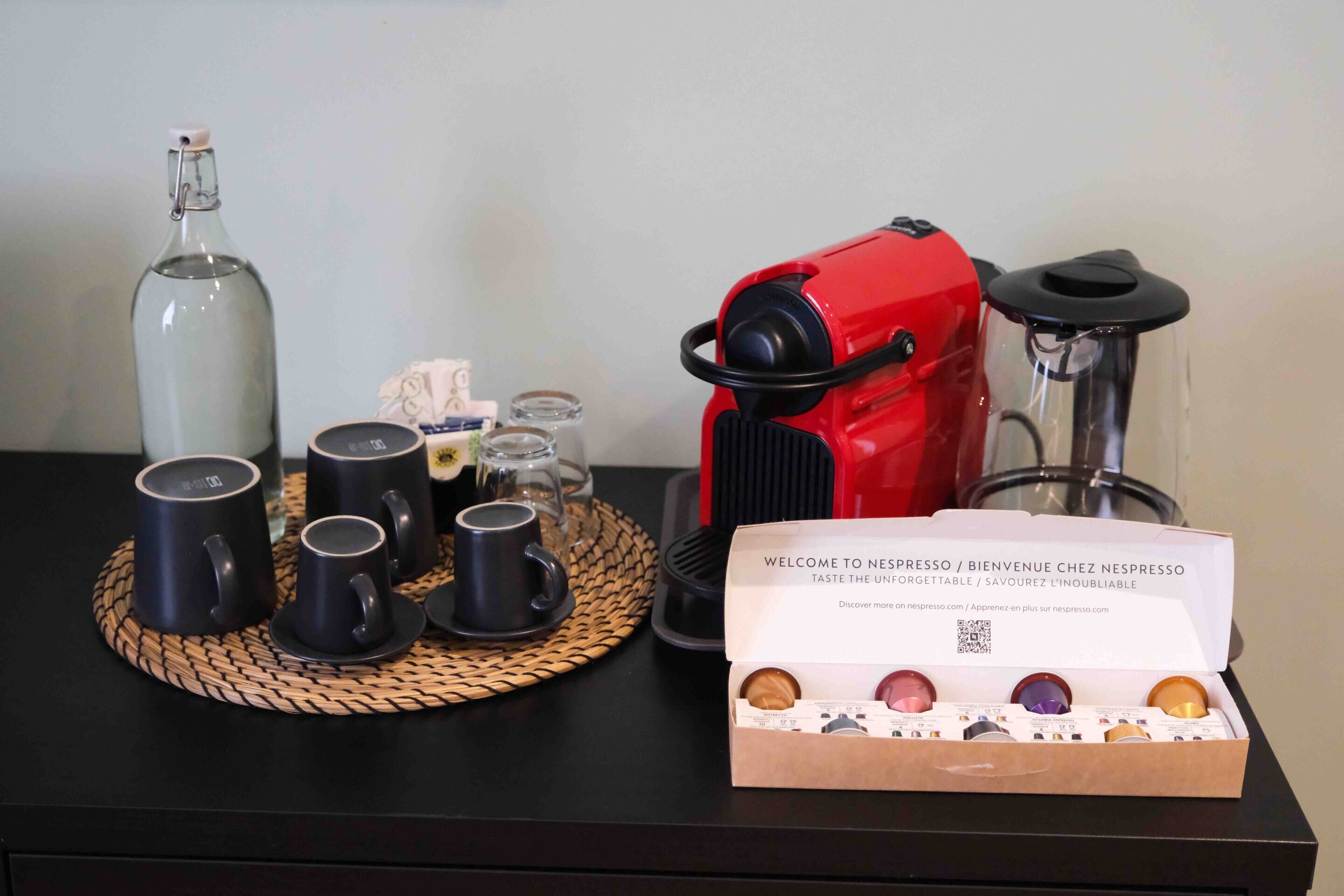 En kaffestation med en röd espressomaskin, en glasflaska och en ask med Nespresso-kapslar på ett svart bord.