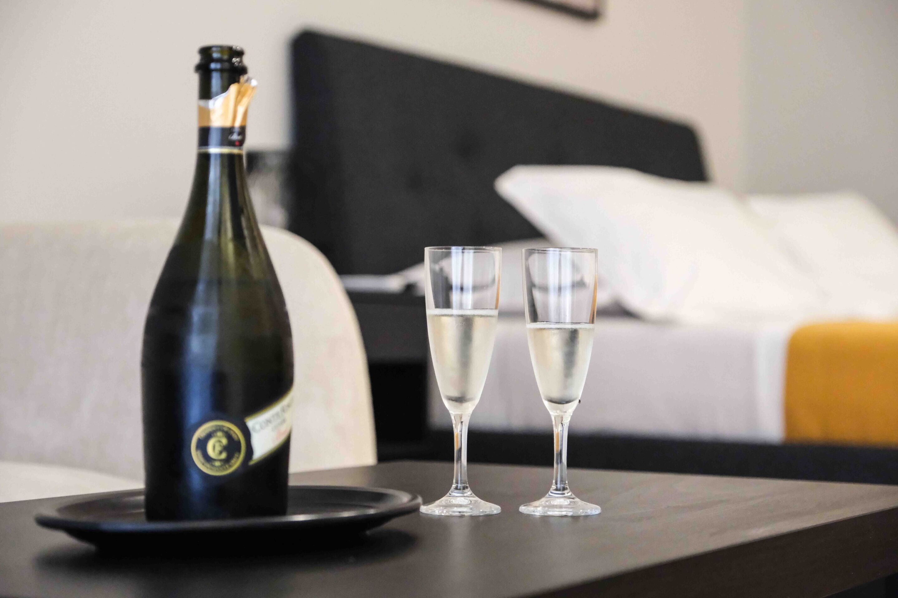 Una botella de champán y dos copas sobre una mesa en una habitación de hotel.