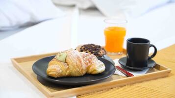 A breakfast tray with a croissant, a glass of orange juice, and a black cup on a bed.