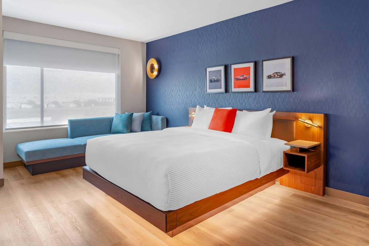 Ein modernes Hotelzimmer mit einem großen Bett, einer Sitzecke, einem Nachttisch und einem Fenster mit Blick.