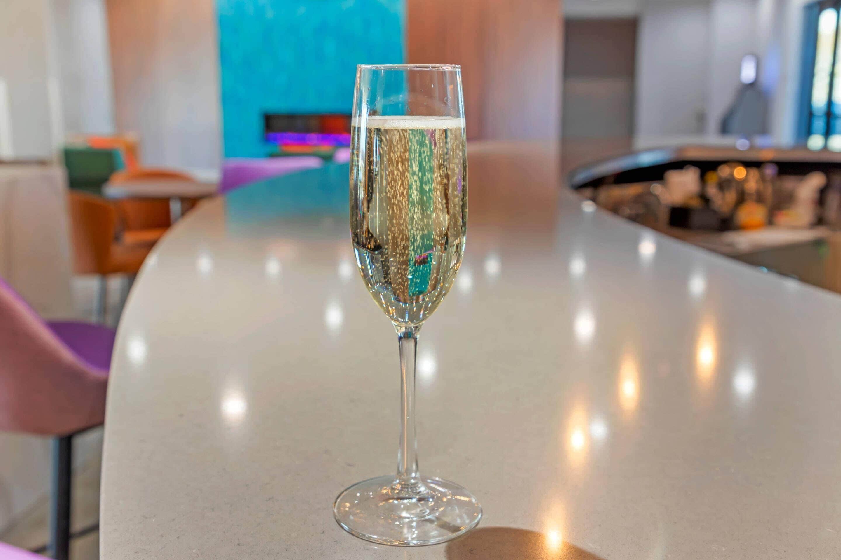 A clear glass of champagne on a bar counter in a modern hotel lobby.