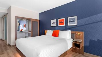 A hotel room with a large bed, a wooden nightstand, a desk, and a wardrobe.
