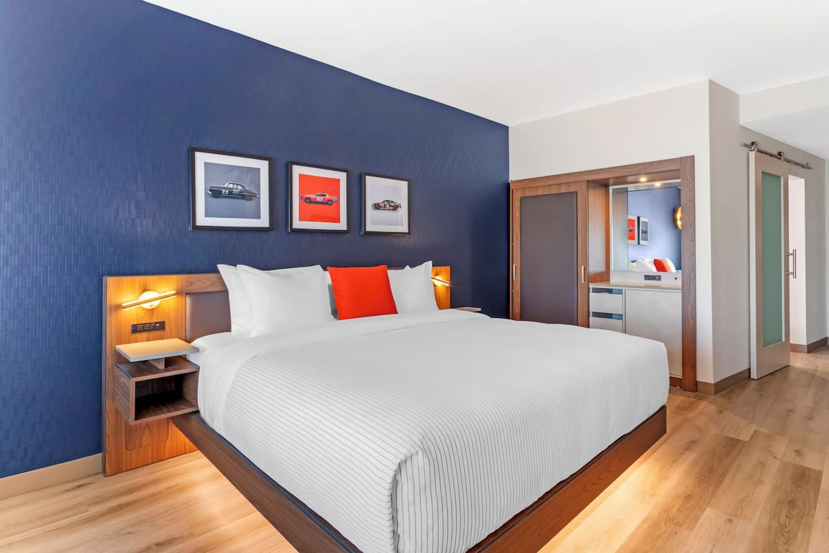 Ein modernes Hotelzimmer mit einem großen Bett, einem Holzkopfstück und einem Nachttisch mit einer Lampe.