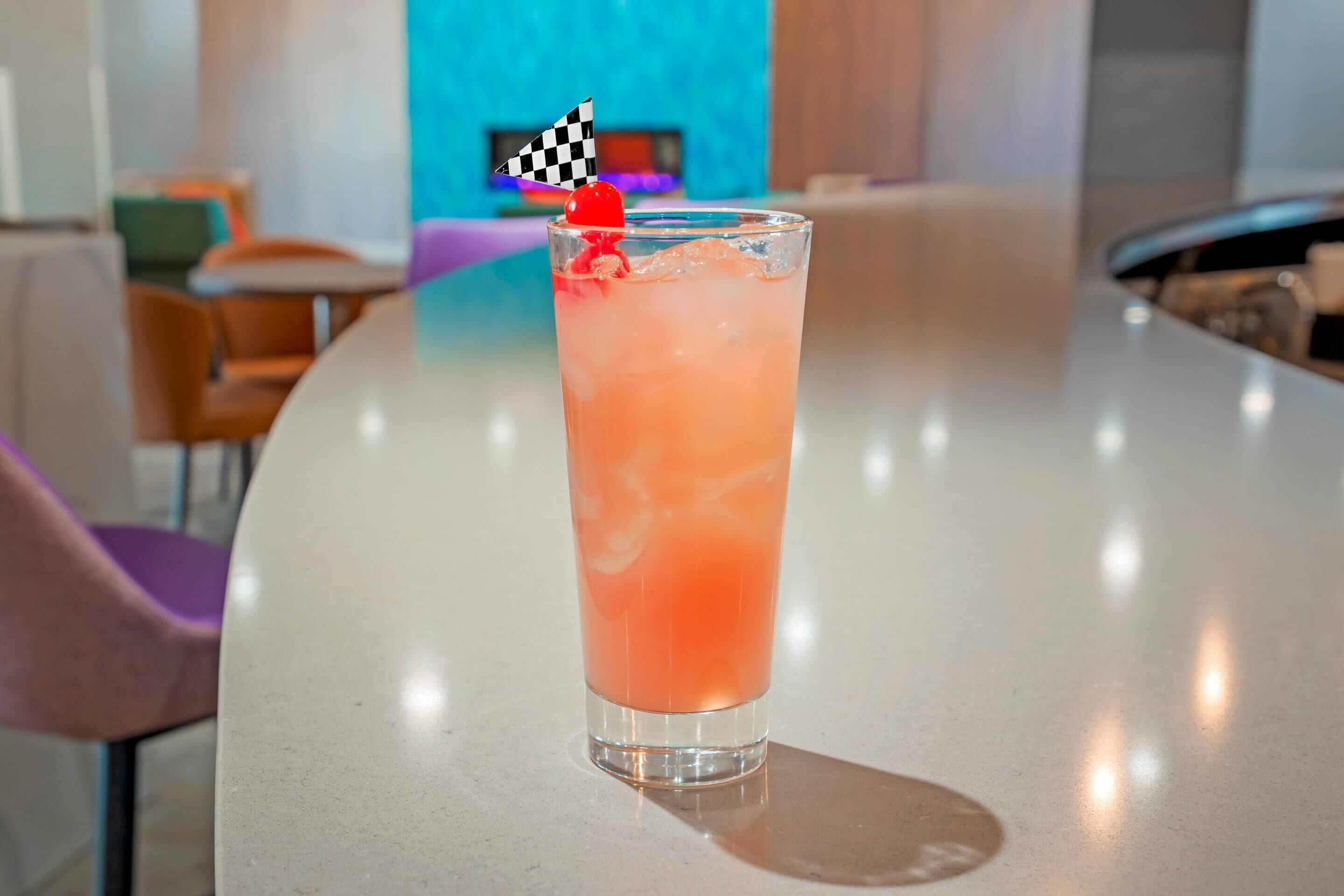Eine Bar mit einem hohen Glas rosa Getränk, einer karierten Zielflagge und einer Kirsche am Rand.