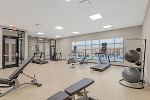 Une salle de sport équipée de matériel d’exercice, dotée de grandes fenêtres et offrant une vue sur la ville.