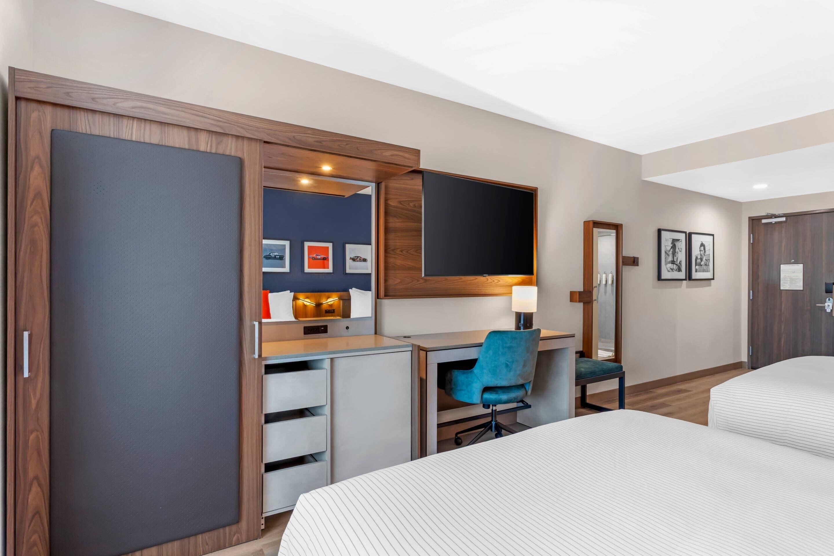 Une chambre d’hôtel comprenant un lit, un bureau avec une chaise, une armoire, un téléviseur et des tableaux encadrés accrochés au mur.