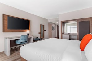 Une chambre d’hôtel avec un grand lit, un bureau avec une chaise, une télévision et une fenêtre.