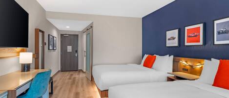 Una habitació d'hotel amb dos llits, una taula de treball amb una cadira, un televisor i quadres penjats a la paret.