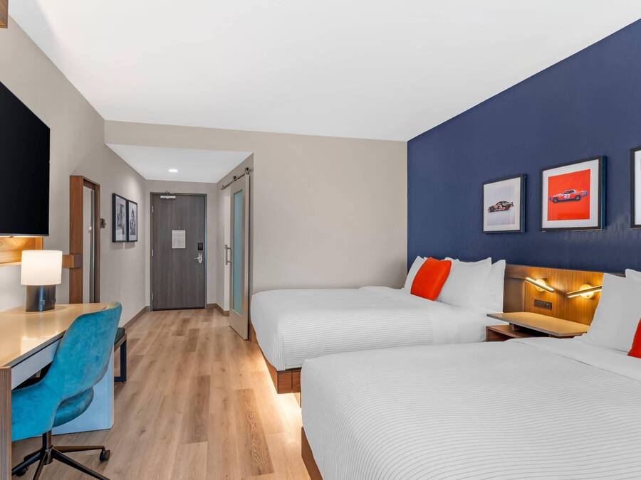 A hotel room with two beds, a desk with a chair, a TV, and framed pictures on the wall.