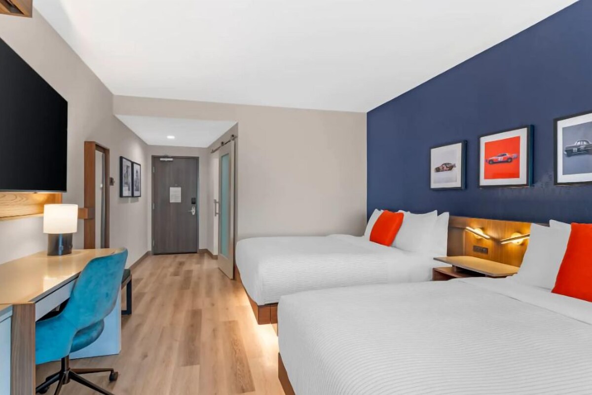 A hotel room with two beds, a desk, and a chair. There are framed pictures on the wall.