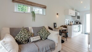 A modern living room with a sofa, a coffee table, and a kitchen in the background. - 1 bedroom accommodation in Faringdon (Faringdon)