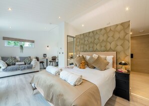 A modern hotel room with a large bed, a desk, a sofa, and a mirror.
