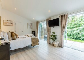 A bedroom with a bed, a TV, a window with curtains, and a plant.