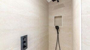 Een moderne douche met een handdouche, een vastgezet rechthoekig douchegarnituur en een bedieningspaneel aan de muur.