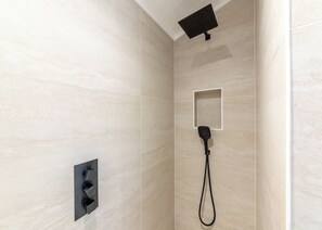 A modern shower with a handheld showerhead, a built-in rectangular showerhead, and a wall-mounted control panel.