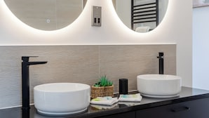 A modern bathroom with two large white sinks, a mirror with integrated lighting, a towel rack, and a small plant on the countertop. - 1 bedroom accommodation in Faringdon (Faringdon)
