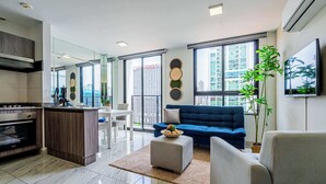 A modern living room with a blue sofa, a dining area, and a kitchen. - w* | Sophisticated 1BR on Calle 50 w/ View (Panamá)