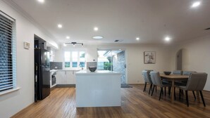 Una cocina moderna con una isla central, un comedor con mesa y sillas, y vistas al exterior a través de un ventanal.