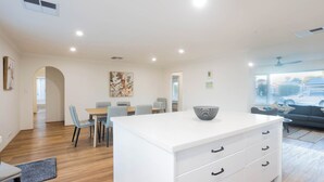 Una sala de estar moderna con una isla blanca, un comedor con sillas y un sofá con vista a la ciudad.