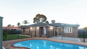 Una casa con piscina, fachada de ladrillo y patio trasero cercado.