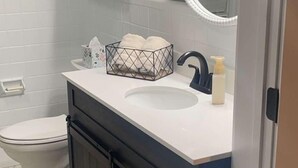 A bathroom with a white sink, dark cabinets, a toilet, and a mirror with a white frame. - Charming 2-bedroom farmhouse in delightful Auburn with AC, WiFi (Auburn)
