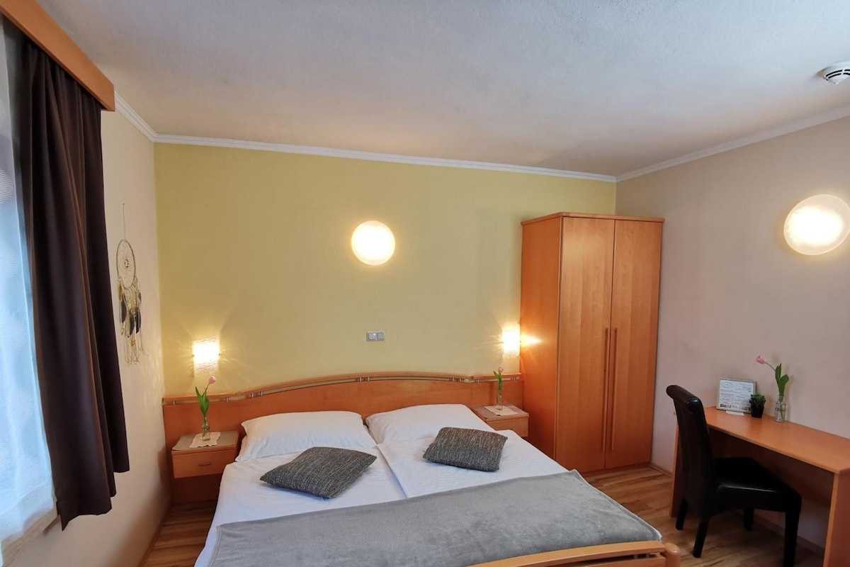 A hotel room with a bed, bedside tables, a desk, and a wardrobe.