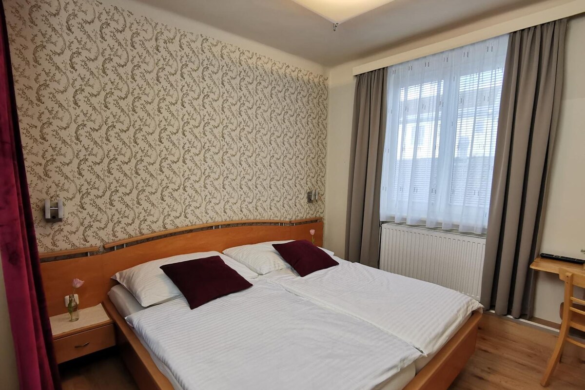A neatly made bed with a wooden headboard, a bedside table with a lamp, and a window with curtains.