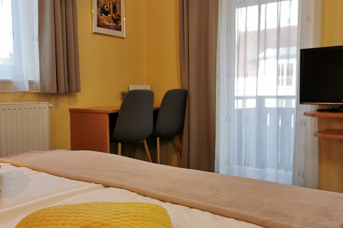 A hotel room with a bed, a desk, two chairs, a television, and a window with curtains.