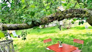 A red metal table and four matching chairs set on a grassy lawn, with a tree branch overhead. - Hotel Wirtshaus Hv Dl Kaplan (Feldbach)