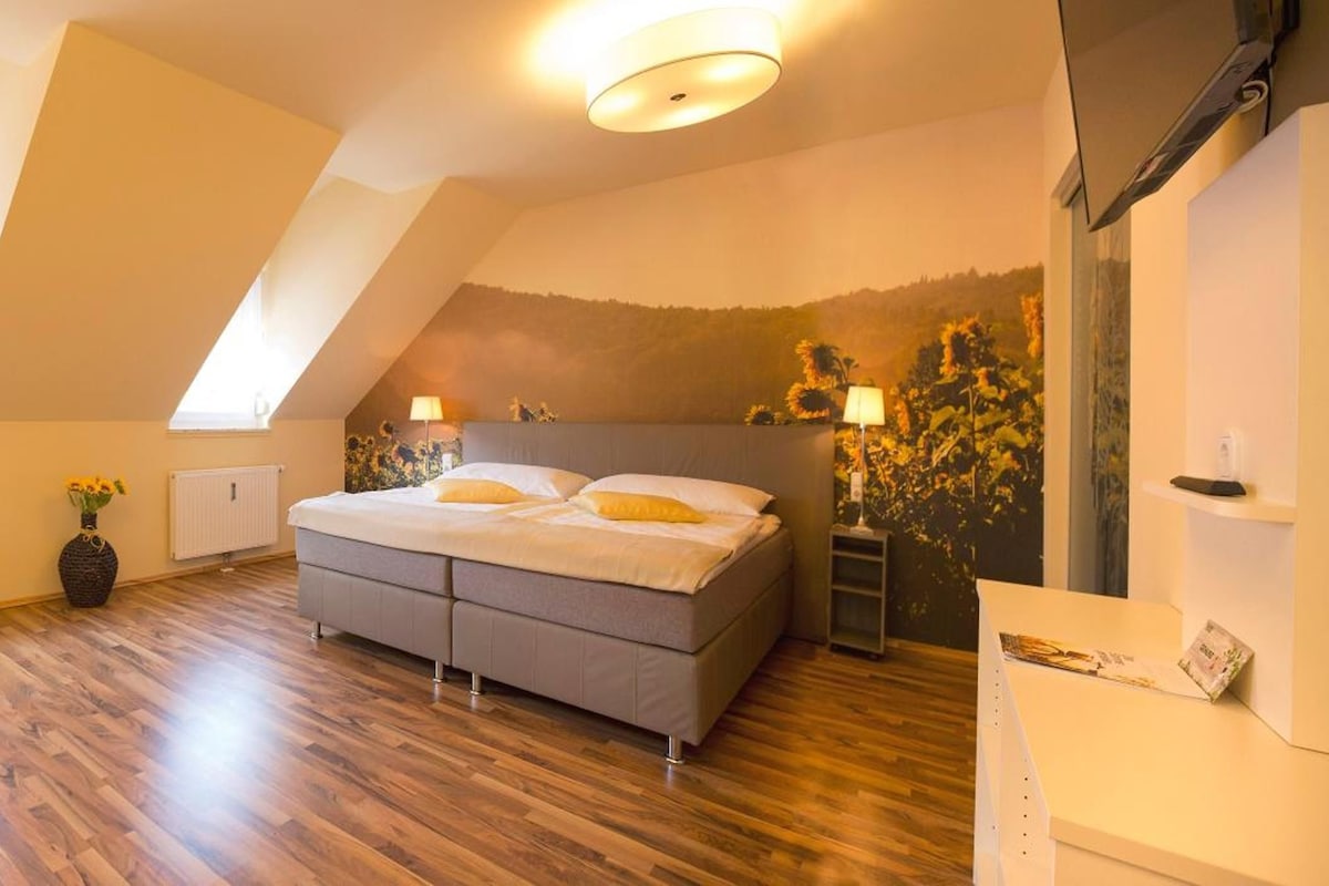 A bedroom with a sloped ceiling, a bed, a radiator, and a wall with a floral mural.