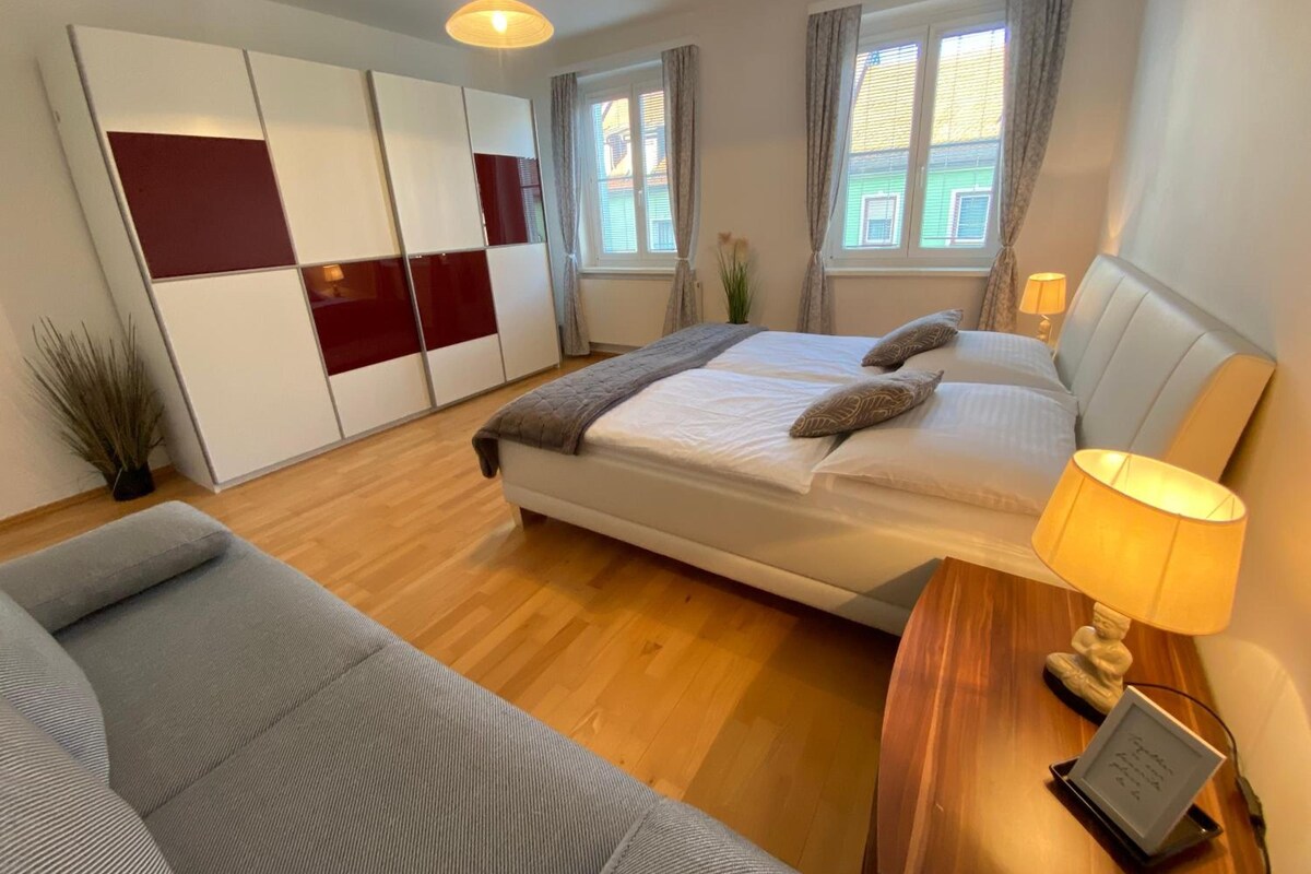 A bedroom with a bed, bedside table, lamp, and a small plant.