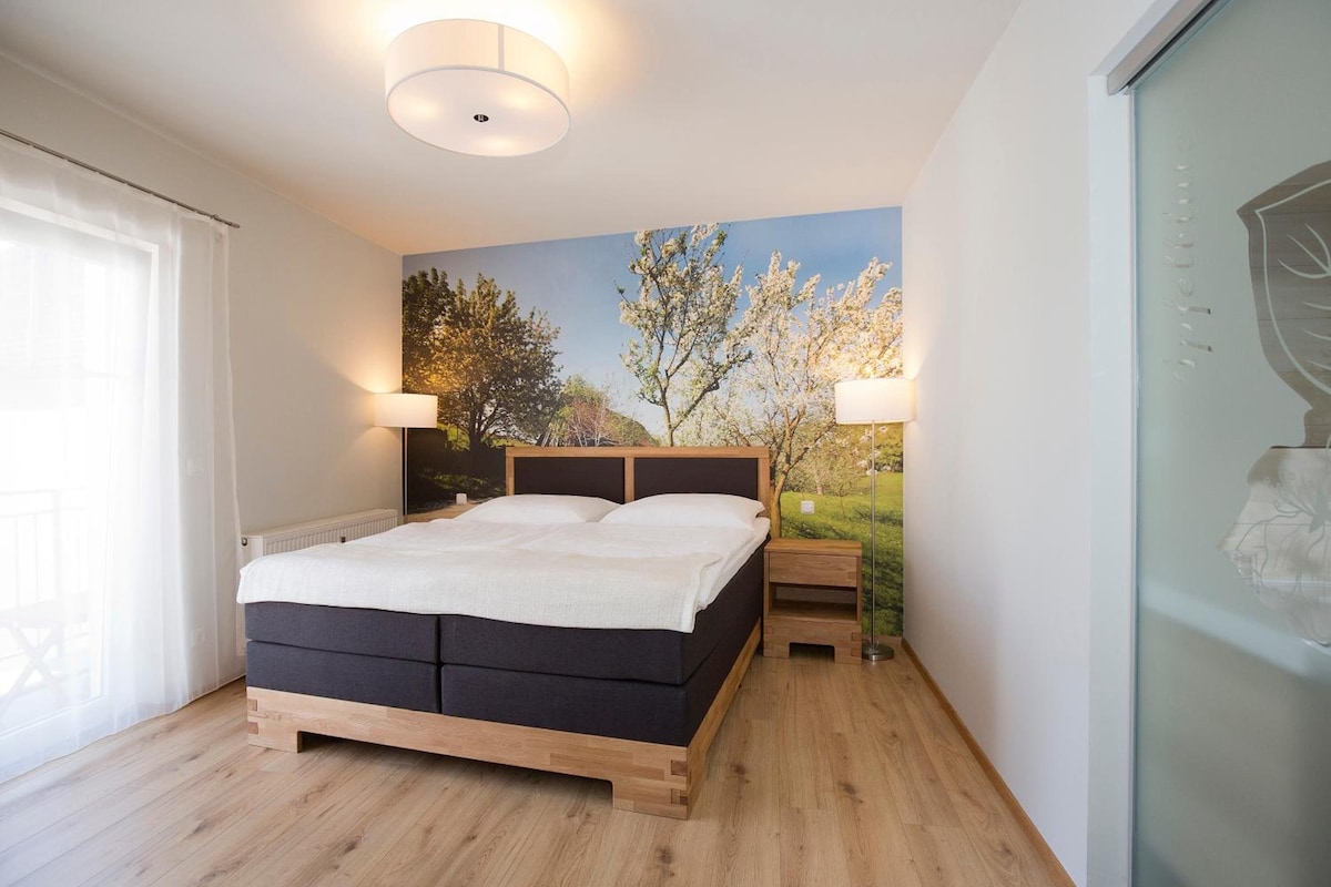 A bedroom with a bed, two bedside lamps, a window, and a wall mural.
