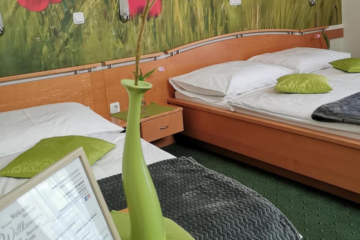 A hotel room with a bed, a bedside table with a vase, and a wall mural of red flowers.